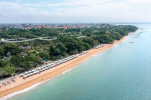 Dronebillede af strand på Sanur med kystlinje og lidt by i baggrunden