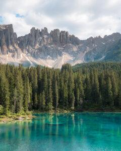 Spektakulær udsigt over Lago di Carezza med smaragdgrønt vand, nåletræer og dramatiske bjergtinder fra Latemar-massivet.